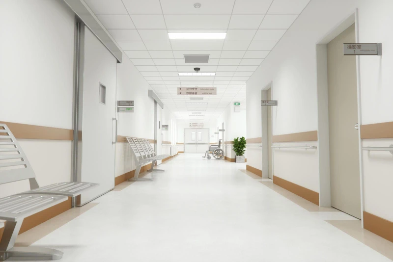 Clean and bright hospital hallway with benches, signs in Japanese, and a wheelchair near the end of the corridor.