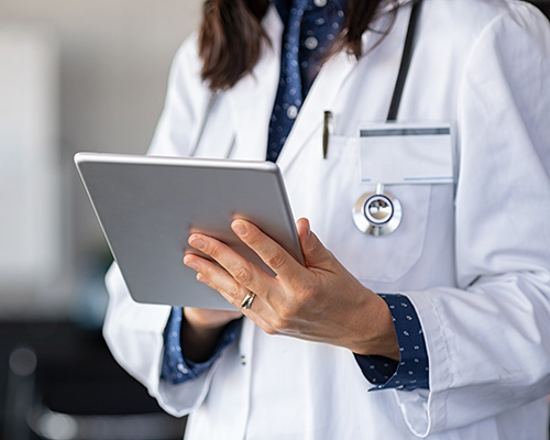 Close up of a female doctor's hands using digital tablet at clinic, reading patient report.