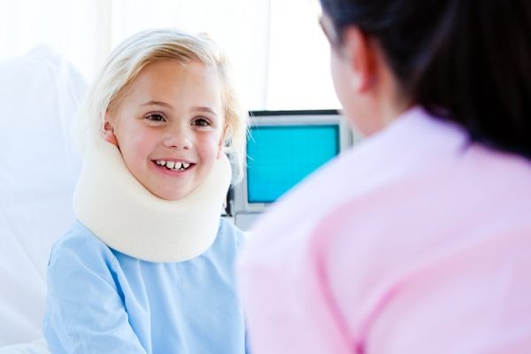 Little girl with a neck brace talking with a nurse sitting on a hospital bed