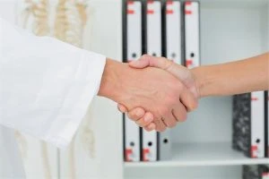 Two hands shaking in a medical office setting.