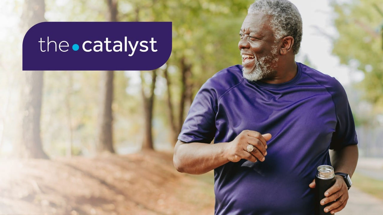 Man running holding a beverage and smiling with trees in the background and the words "the catalyst" in the top left corner.
